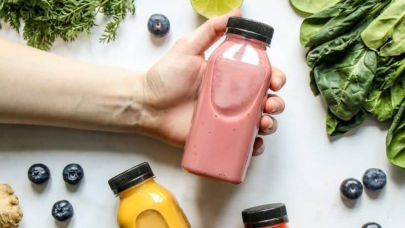 Person Holding Bottle of Smoothie Beside Green Leaves, Carrots and Berries
